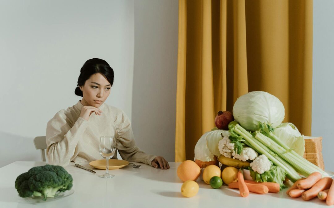 A woman seated at a table with a variety of fresh vegetables, representing healthy eating.