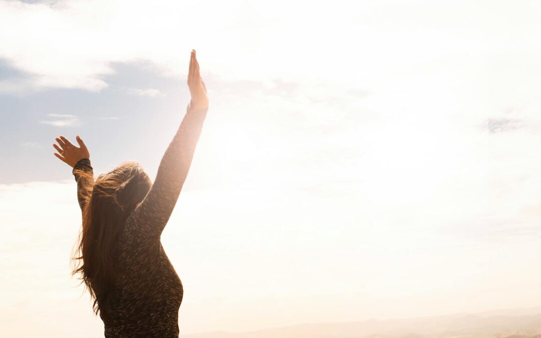 A woman with raised arms enjoying the bright open sky in a serene outdoor setting.